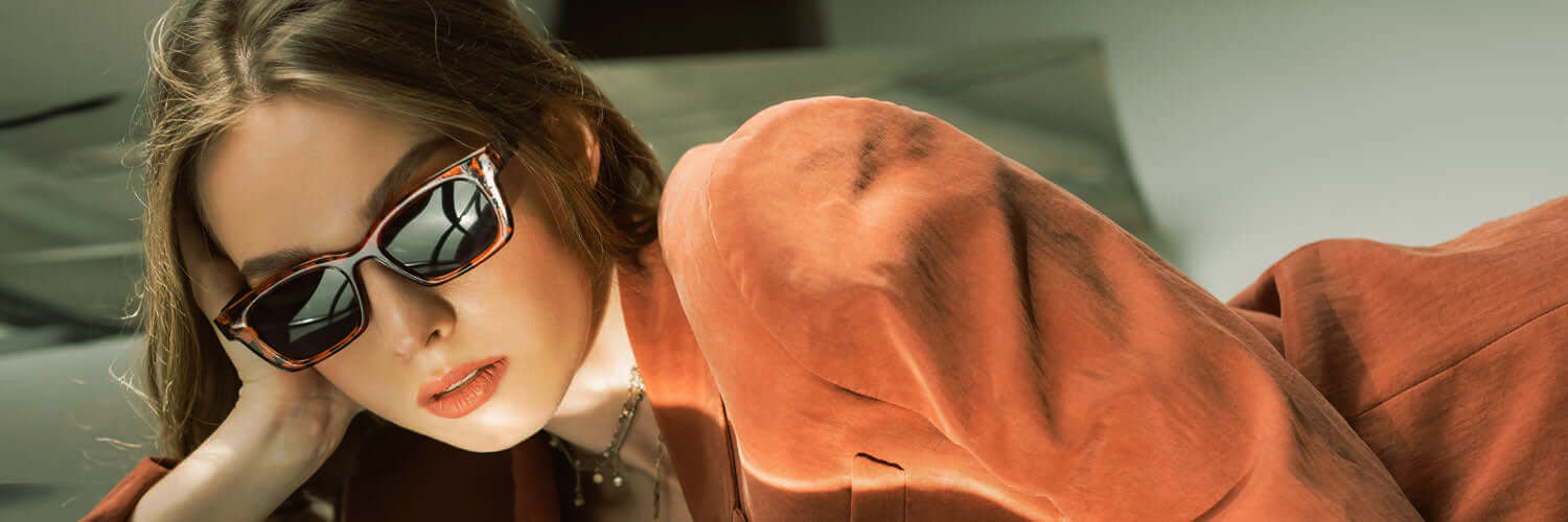 brunette hair woman laying down with hand to face wearing tortoise shell sunglasses and maroon blazer