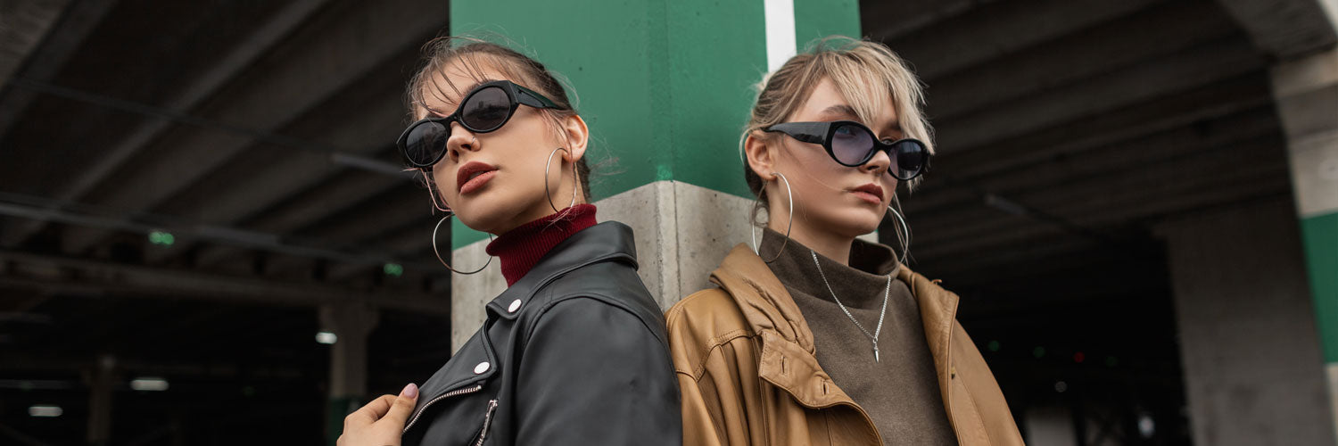 two females standing in front of a parking structure wearing sunglasses looking in opposite directions