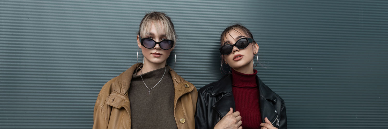 Two women wearing sunglasses against a textured wall.